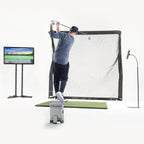 Person practicing golf swings on a simulator with a screen displaying a golf course.