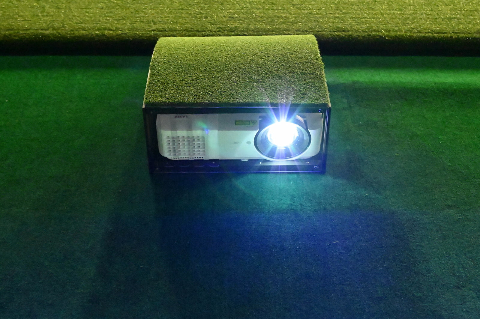 Small projector on a green surface with a bright light shining.