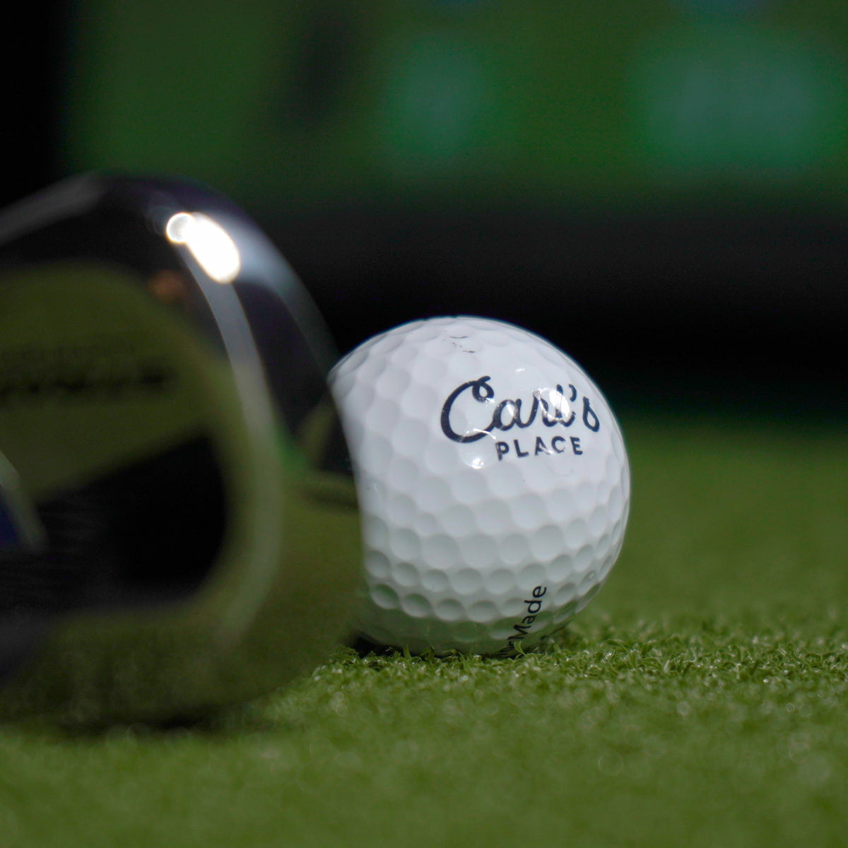 Golf ball with 'Carls Place' branding on a green surface, close-up.