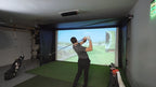 Person practicing golf swings in a home indoor simulator setup.