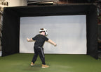 Person wearing a virtual reality headset in front of a white screen with black curtains on either side.