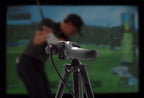 Golf simulator setup with a screen displaying a golf course and a camera on a tripod.