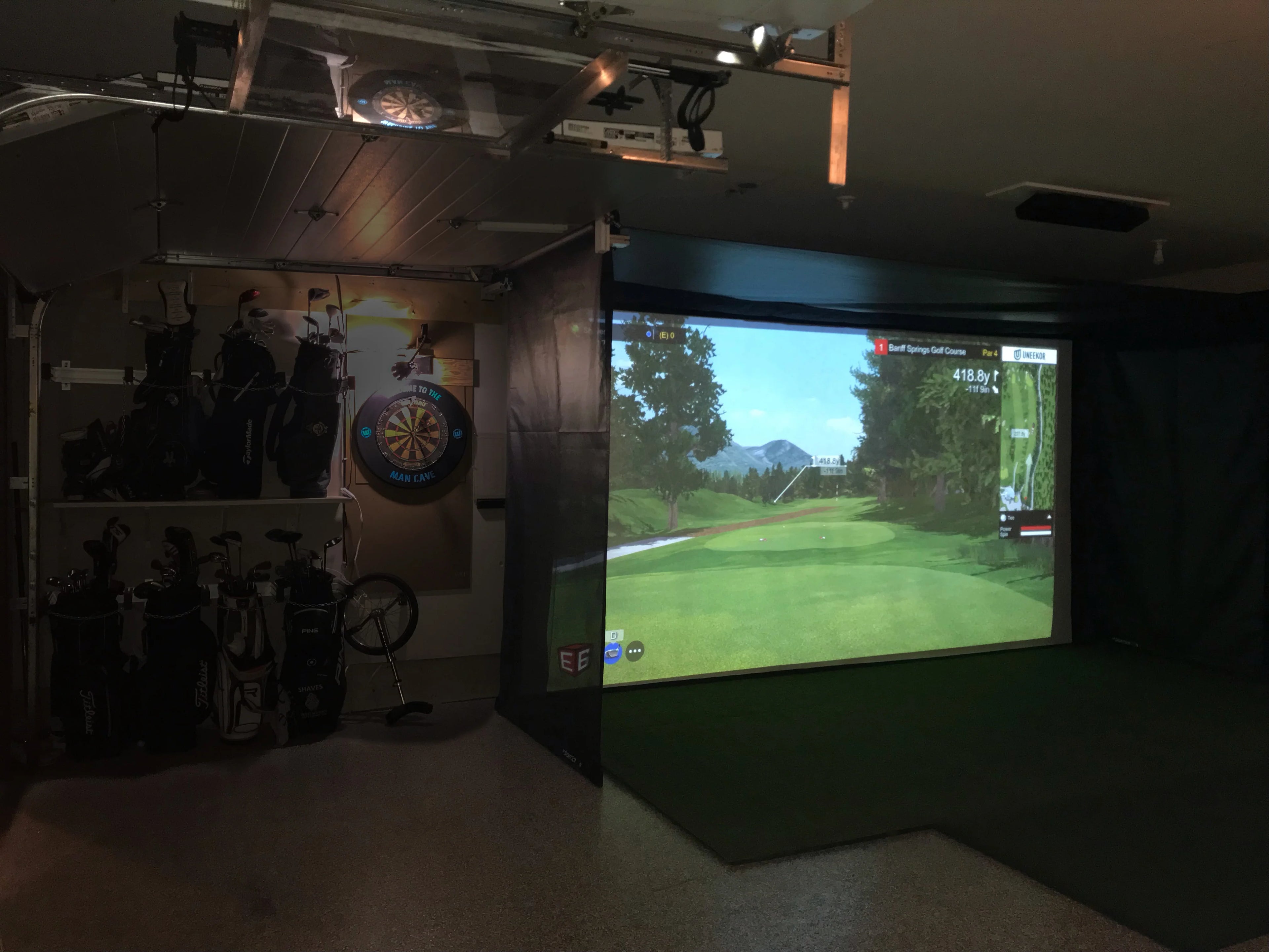 Indoor golf simulator setup with screen displaying a golf course.