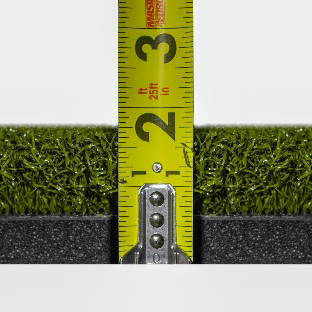 Measurement of artificial grass with a tape measure showing 2.5 feet.