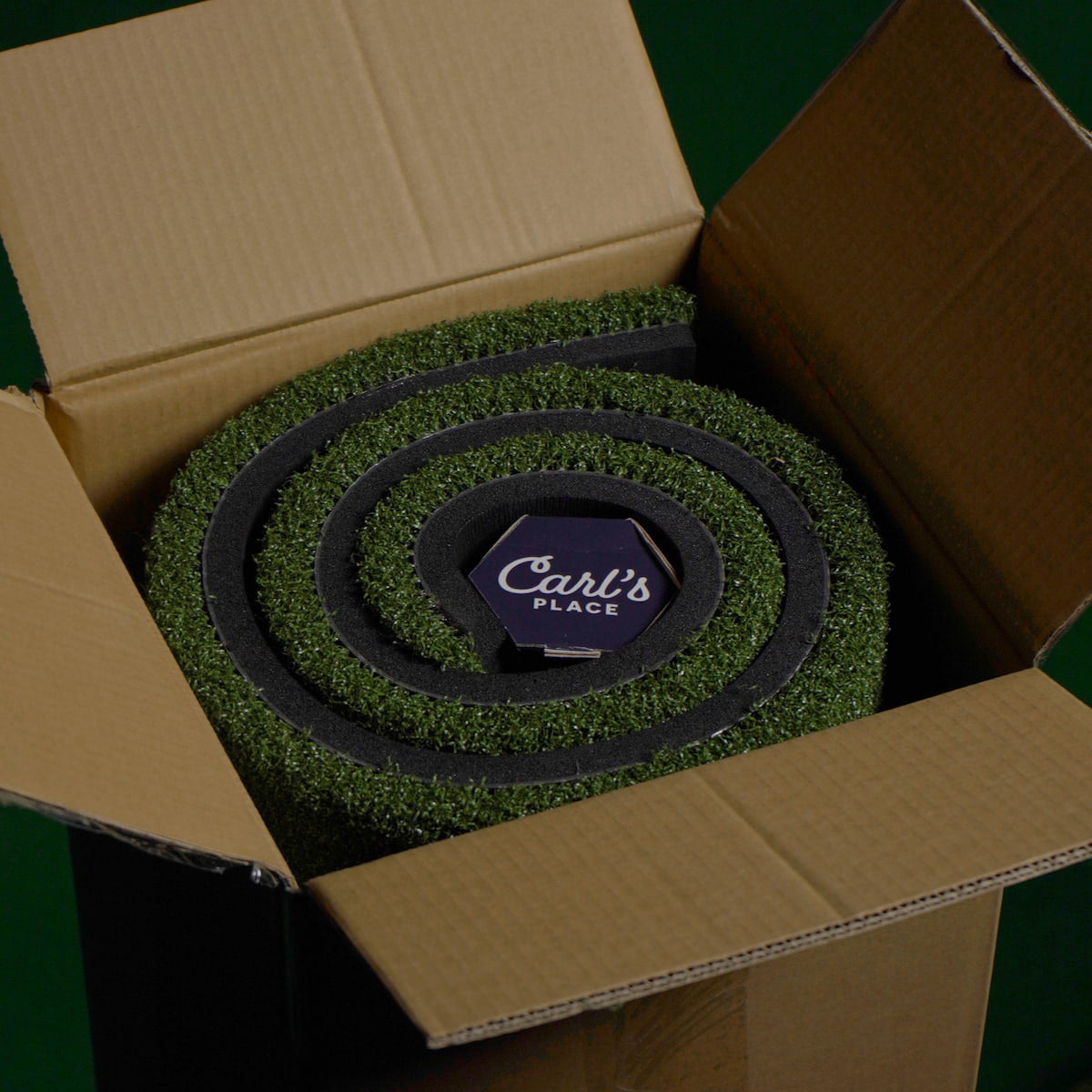 Green roll of carpet with 'Carl's Place' logo in an open cardboard box.