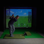 Man practicing golf swings in a simulator setup with a screen displaying a golf course.