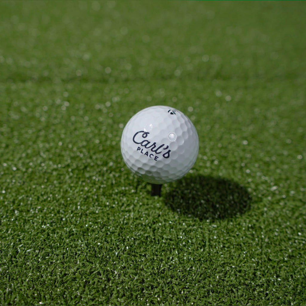 Golf ball with 'Carl's Place' branding on a green grass surface
