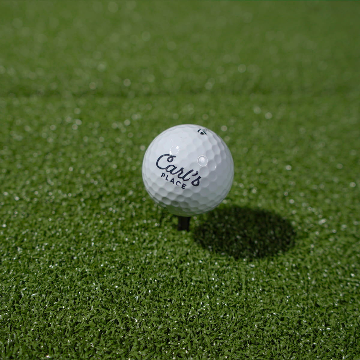 Golf ball with 'Carl's Place' branding on a green grass surface
