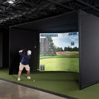 Person playing golf in a virtual reality simulator with a screen displaying a golf course.