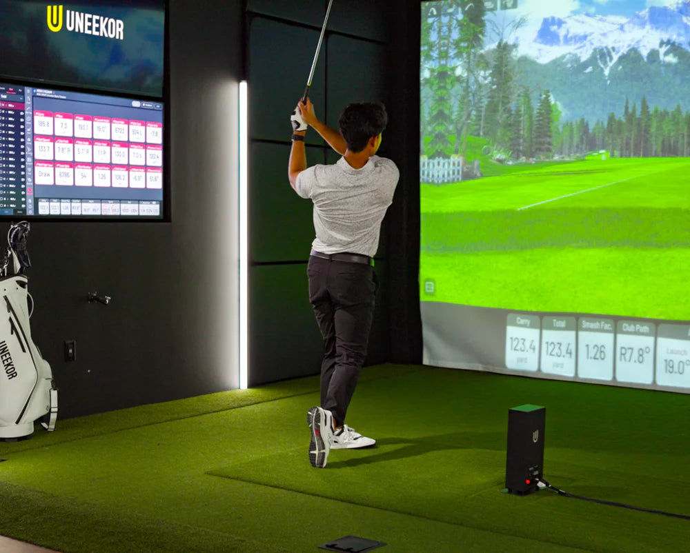 Person practicing golf swings in a模拟器环境 with UNEEKOR branding.