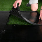 Person adjusting a black folding chair on artificial grass