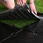 Person adjusting a black plastic grid on artificial grass
